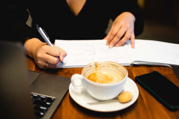 Hand writing in a journal next to a cup of coffee